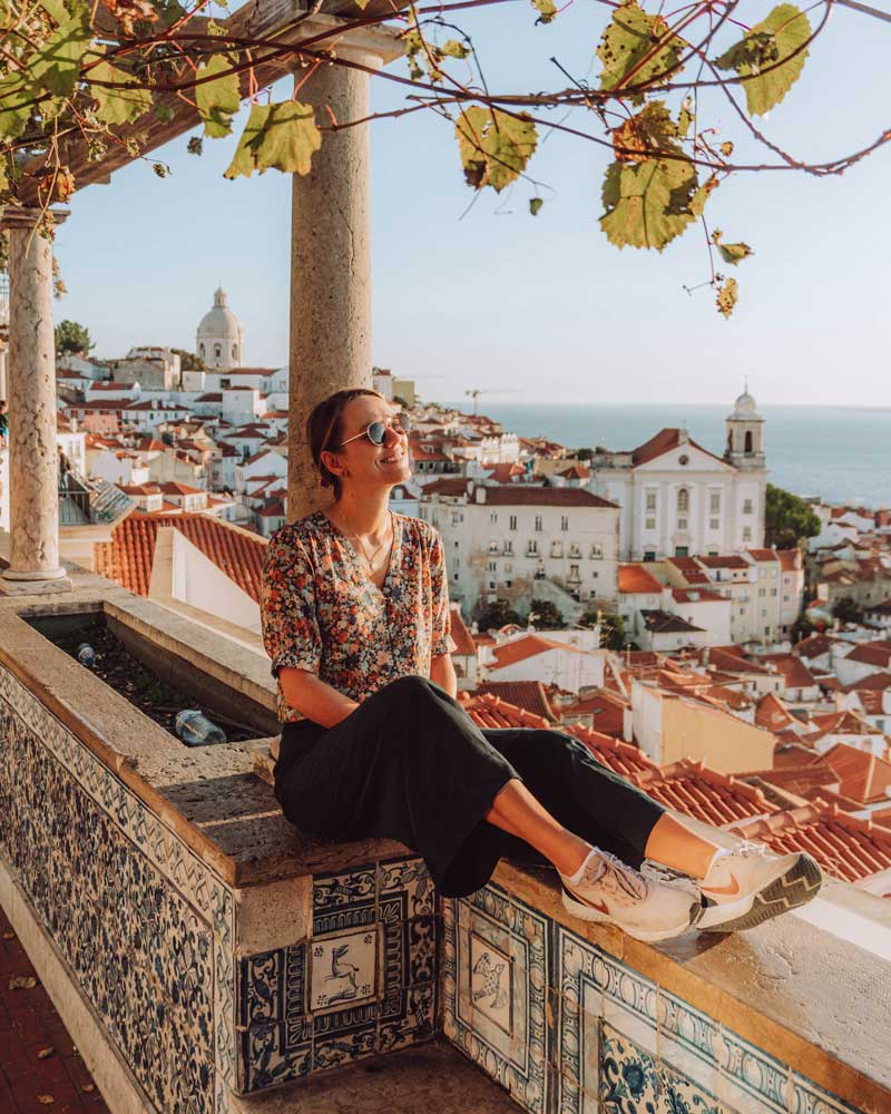 Woman sitting at a wall enjoying the view from a viewpoint in Lisbon